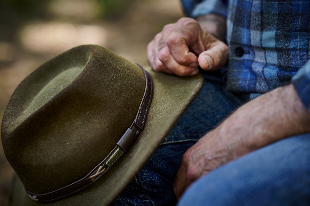 A close-up of a faded dark green hat with a wide brim, with one hand resting on top of it.