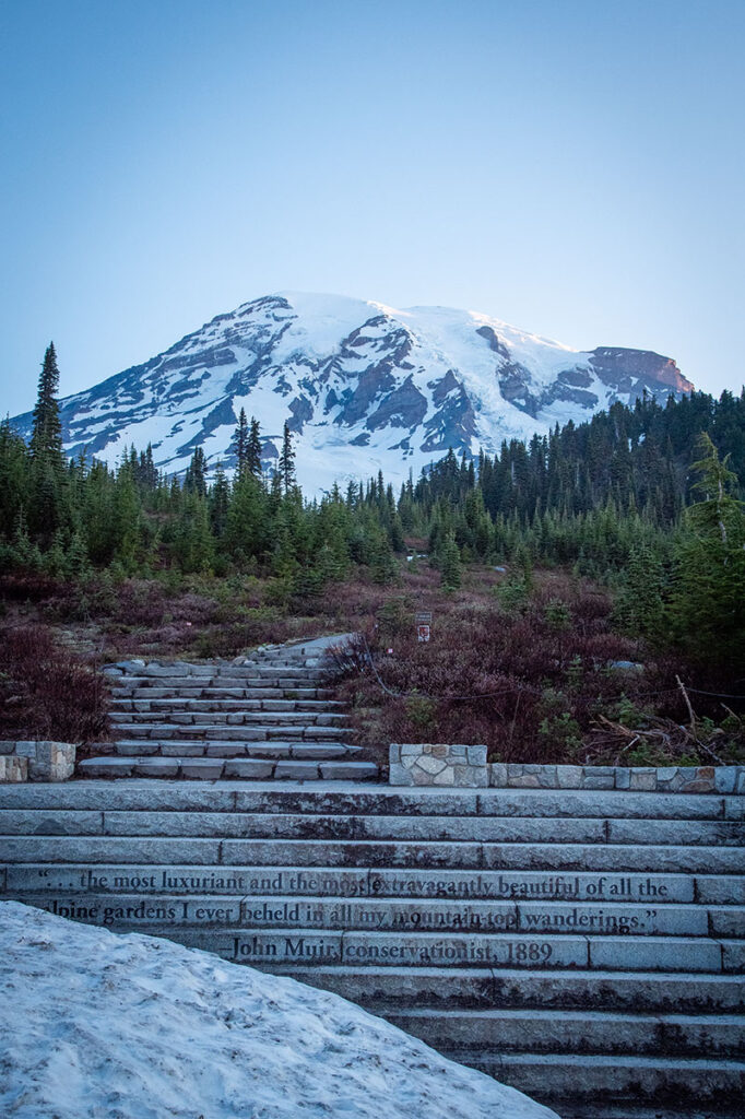 Snow sits on top of the mountain in the foreground, with a concrete staircase leading up a pathway.