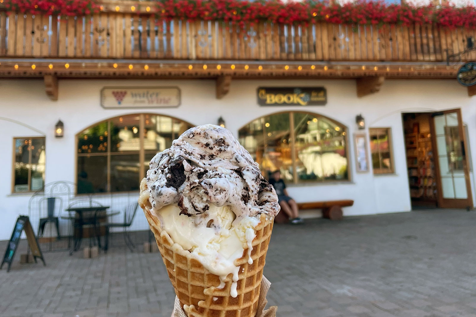 Melting ice cream in a waffle cone is held up in front of shops