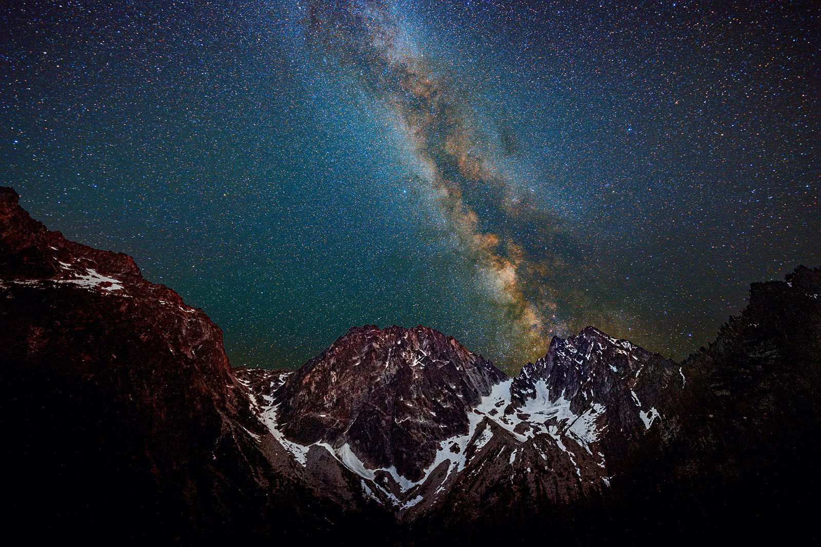 The Milky Way and lots of stars are seen over the tops of snow-covered mountains.