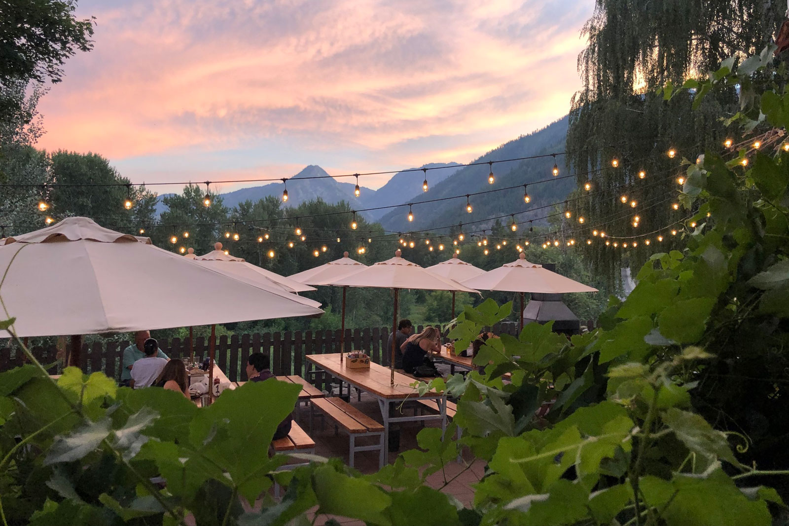 Picnic tables beneath market lights are nestled among the mountains under a sky full of pink clouds.